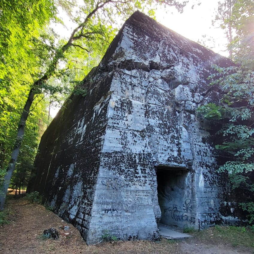 Bunkier Himmlera Hochwalda na Mazurach, otoczony drzewami – historyczna atrakcja na trasie Zamek w Rynie na Mazurach, historyczna budowla otoczona brukowanym placem – atrakcja w regionie Mazurskiej Pętli Rowerowej..
